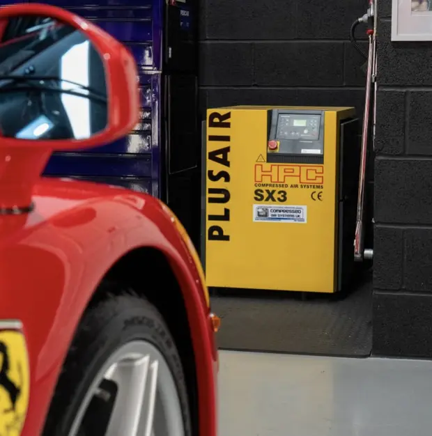 A yellow air compressor installed inside the ALC Elite workshop, with the wing of a red Ferrari in the foreground