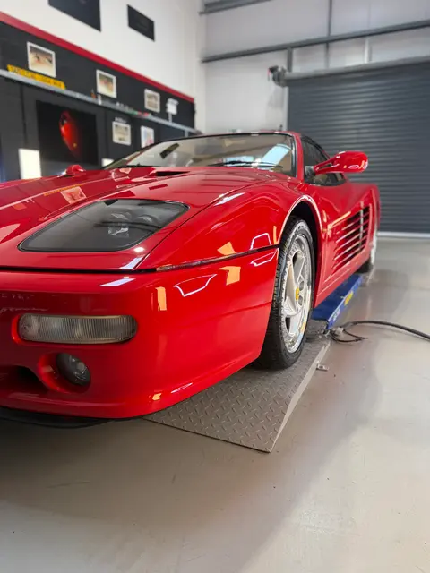 A red sports car in the ALC Elite workshop, with interior, engine bay and wheels away from the car