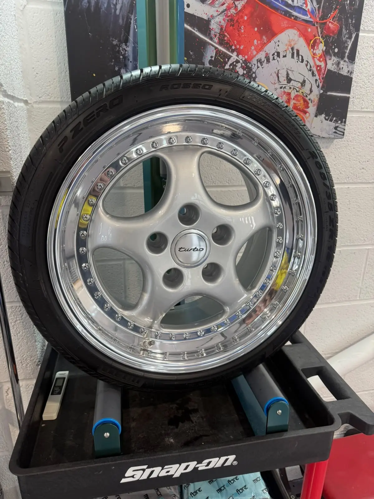 A Porsche Turbo split-rim wheel with a mirror-polished lip and fitted tyre, on a workshop trolley