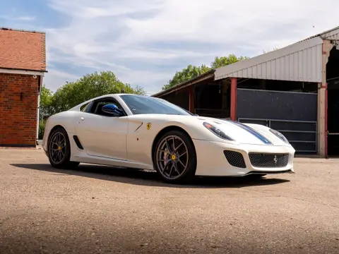 A white sports car with a blue stripe, photographed outside on a brick courtyard
