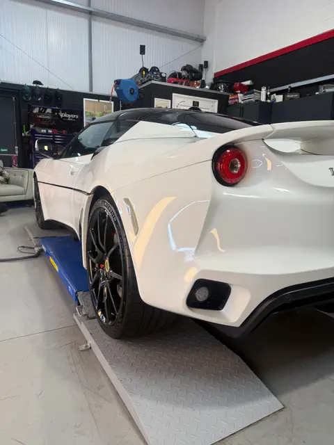 The rear three-quarter of a white Lotus Evora on a ramp in the ALC Elite workshop